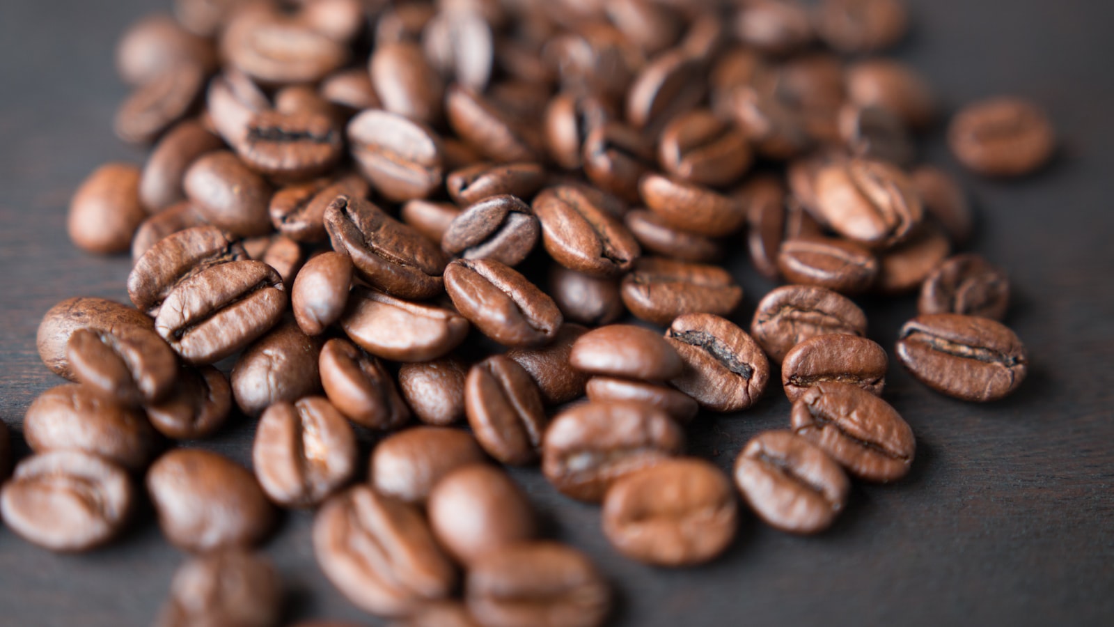 A bag of whole coffee beans with beans spilling onto a table